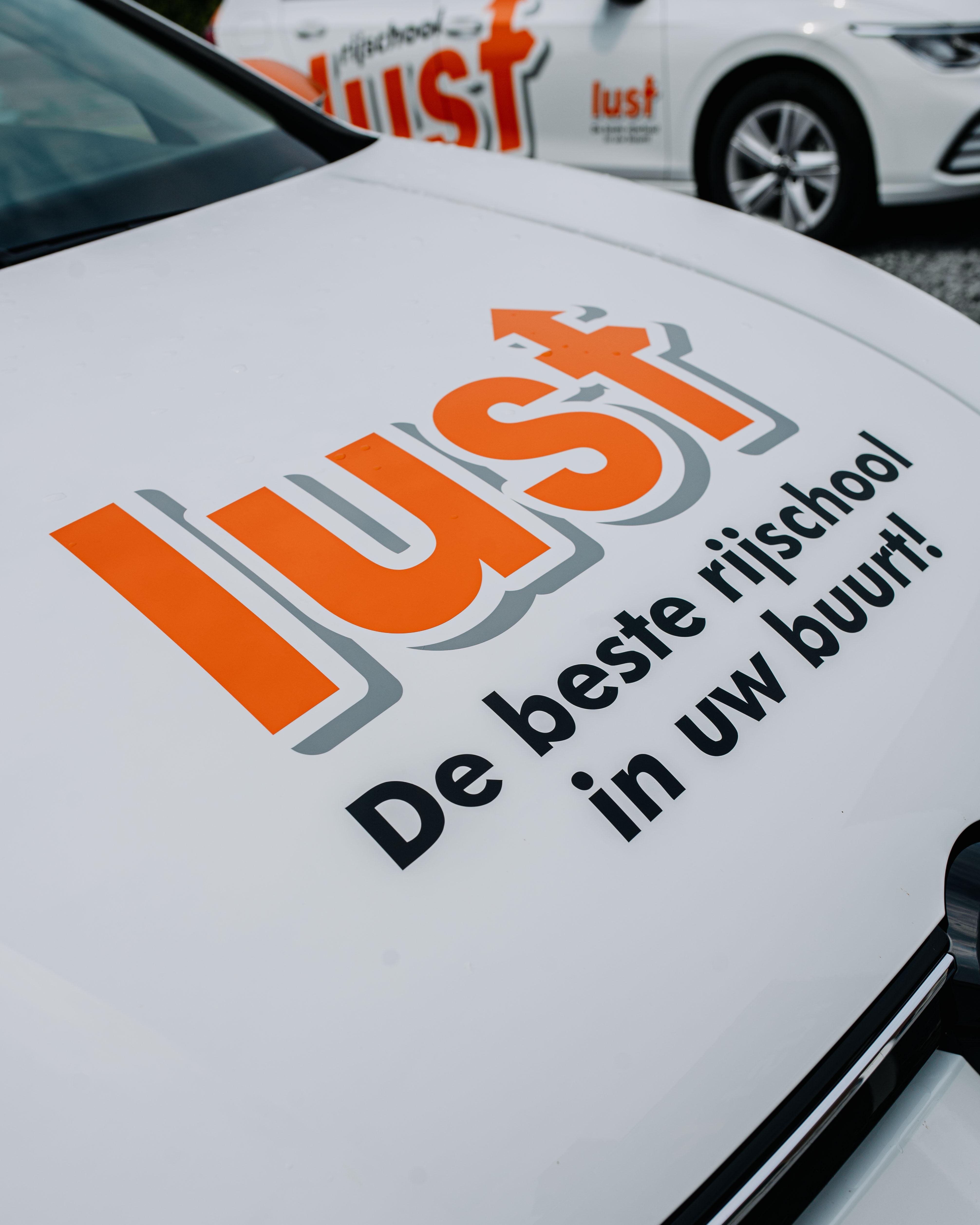 Close-up van een witte motorkap met daarop het Lust Rijscholen logo op